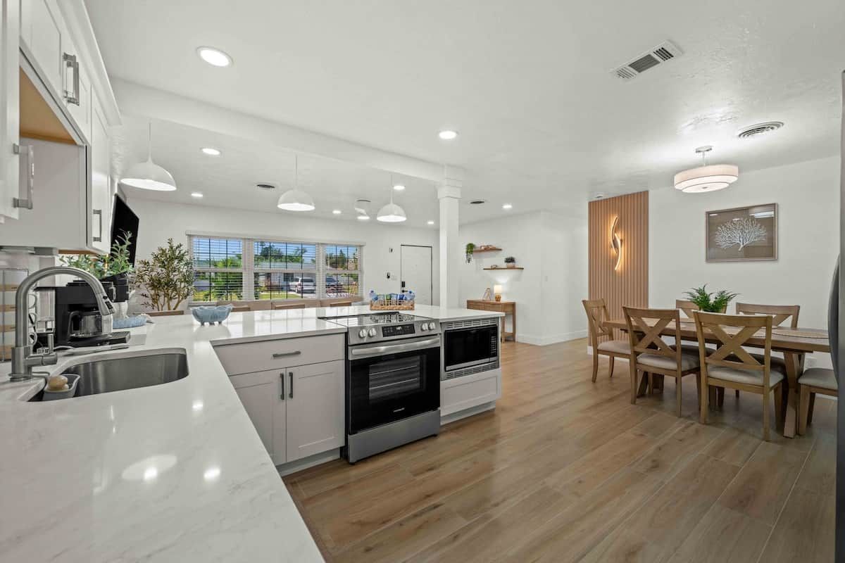 A modern kitchen with a central island, built-in oven, and a dining area with wooden chairs.