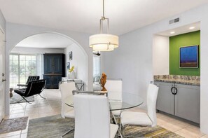 Zona pranzo moderna con tavolo in vetro, sedie bianche e lampadario a sospensione.