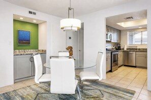 A modern kitchen with stainless steel appliances, a dining area with a glass table and white chairs, and a green accent wall. - Mesquite Mountain Retreat Phase 3 (Palm Springs)