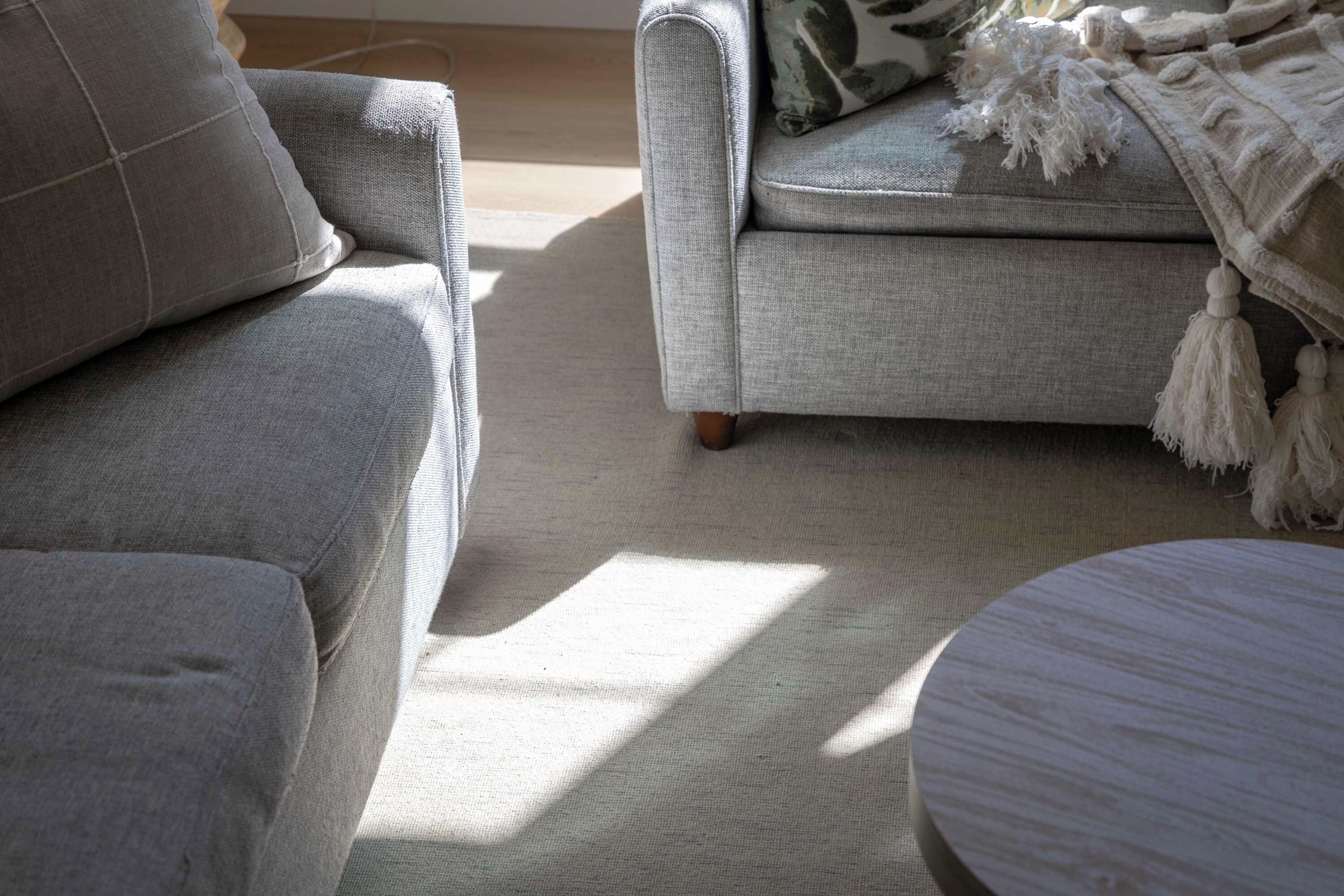 Un salon avec un canapé gris, un fauteuil assorti et une table basse ronde.