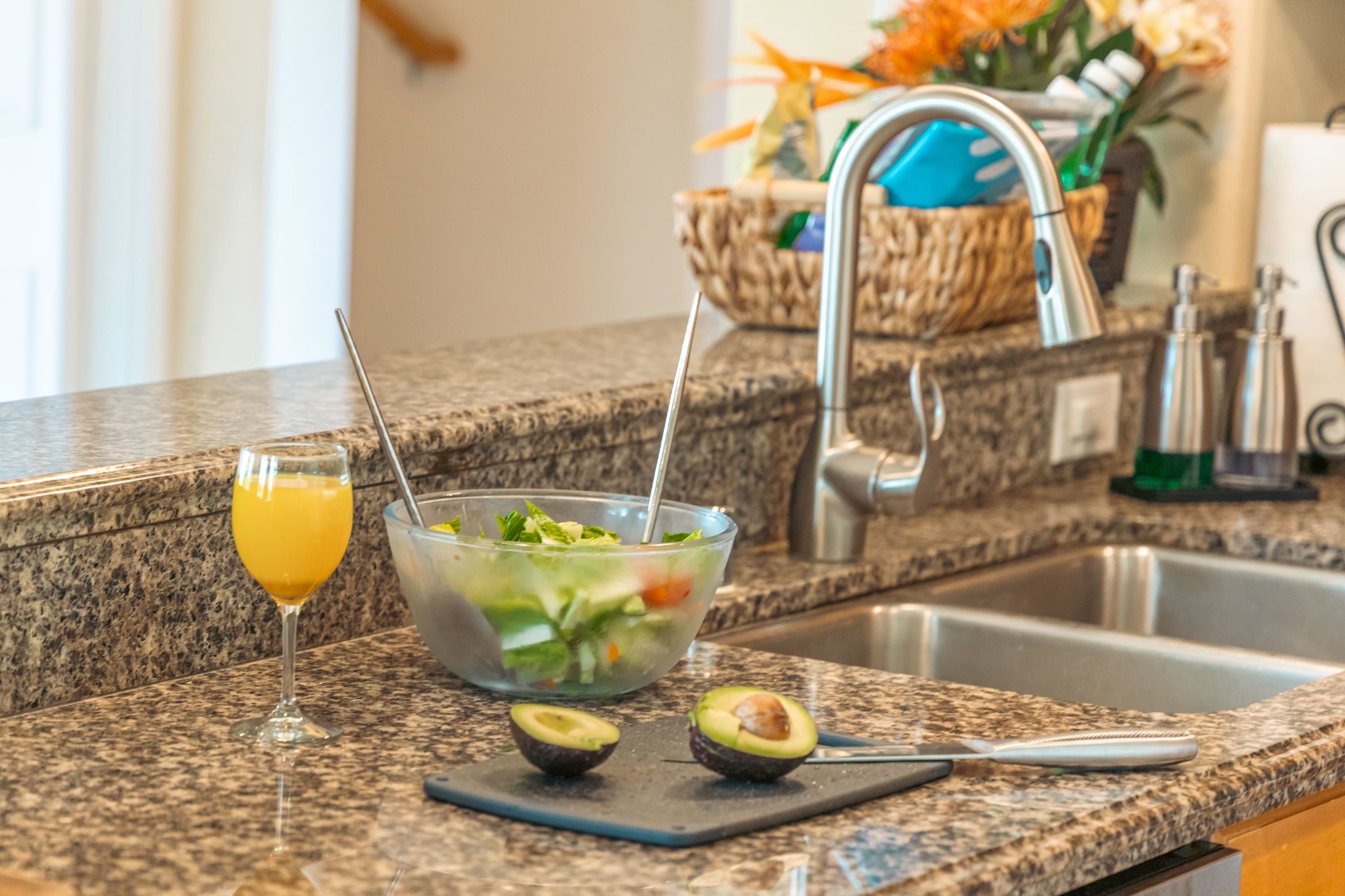 Un comptoir de cuisine avec un verre de jus d’orange, un saladier rempli de salade et deux moitiés d’avocat sur une planche à découper.