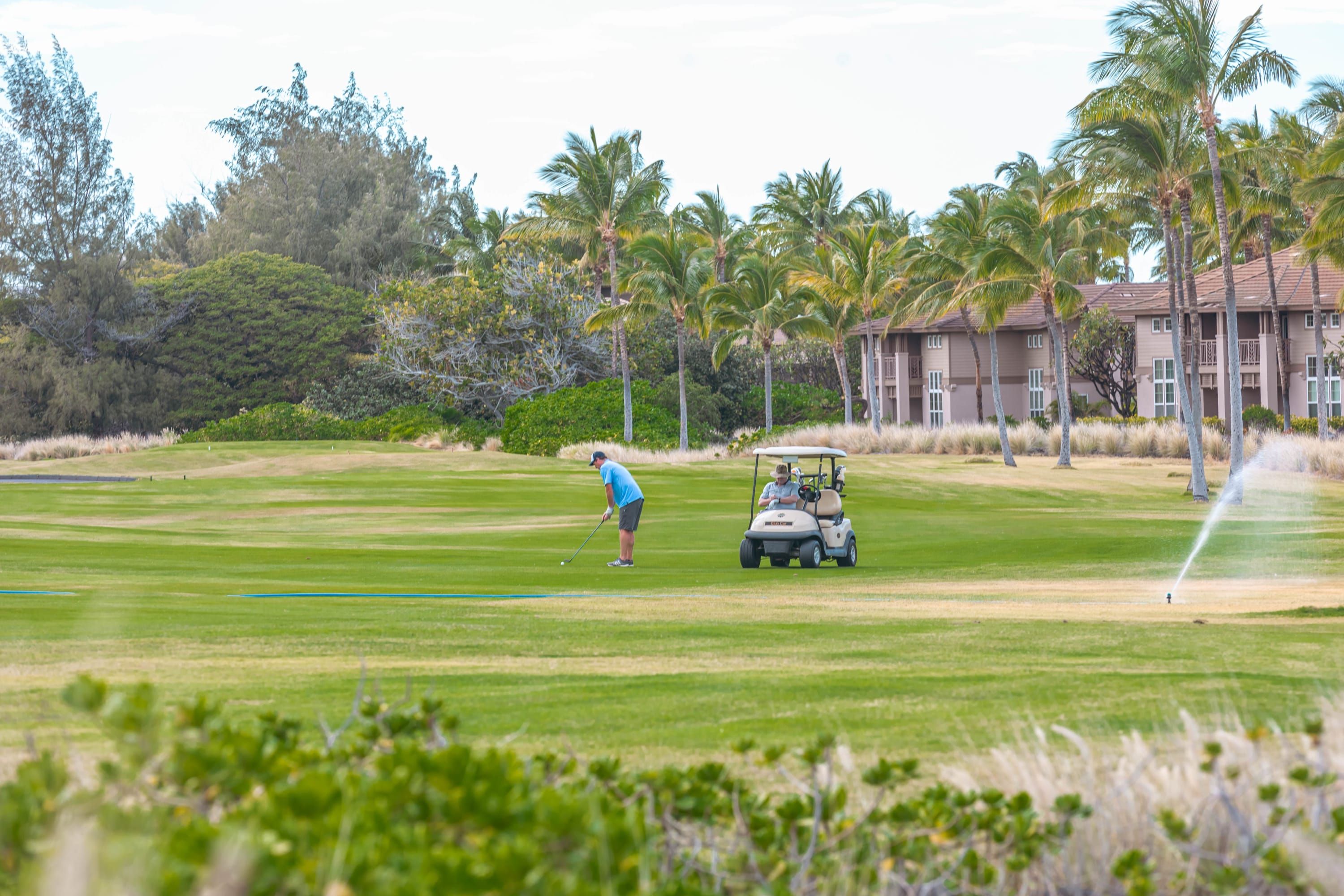 Un campo de golf con una persona a punto de colocar la bola, un carrito de golf y un edificio al fondo.