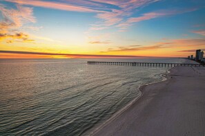 A beach with a pier extending into the water, a clear sky, and a sunset. - Easy Breezy with Gulf Views and walk to Pier Park (Panama City Beach)