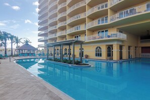 Un hôtel doté d’une piscine, de nombreux balcons et d’un espace extérieur couvert avec des chaises et des parasols.