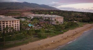Hotel a la costa amb diverses edificacions, una platja i un paisatge de muntanyes al fons.