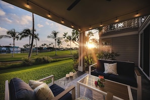 A covered outdoor seating area with a view of a golf course and palm trees. - Hilton Pool Pass 2026-27 | Sunset Family Villa 3bd (Waikoloa Village)