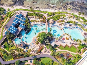 A resort with multiple swimming pools, palm trees, and a large building with a blue roof. - Hilton Pool Pass 2026-27 | Sunset Family Villa 3bd (Waikoloa Village)