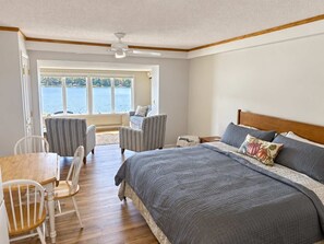 A bedroom with a large bed, a desk, two chairs, and a view of a lake. - Clam Lake Terrace Retreat (Bellaire)