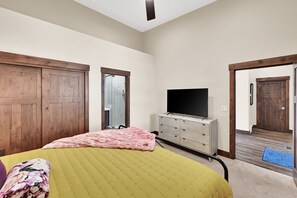 Quarto com uma cama, televisão, penteadeira e porta que dá para outro cômodo.