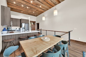 A modern kitchen with a wooden ceiling, stainless steel appliances, and a dining area with a wooden table and blue chairs. - Stunning Townhome Mountain Views and Amenities (Eden)