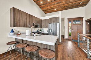 A modern kitchen with a central island, bar stools, stainless steel appliances, and a wooden ceiling. - Stunning Townhome Mountain Views and Amenities (Eden)
