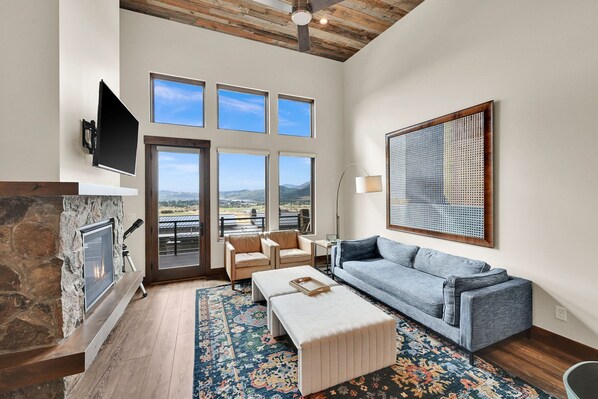 A spacious living room with a fireplace, a large sofa, a coffee table, and a view of the outdoors through multiple windows. - Stunning Townhome Mountain Views and Amenities (Eden)
