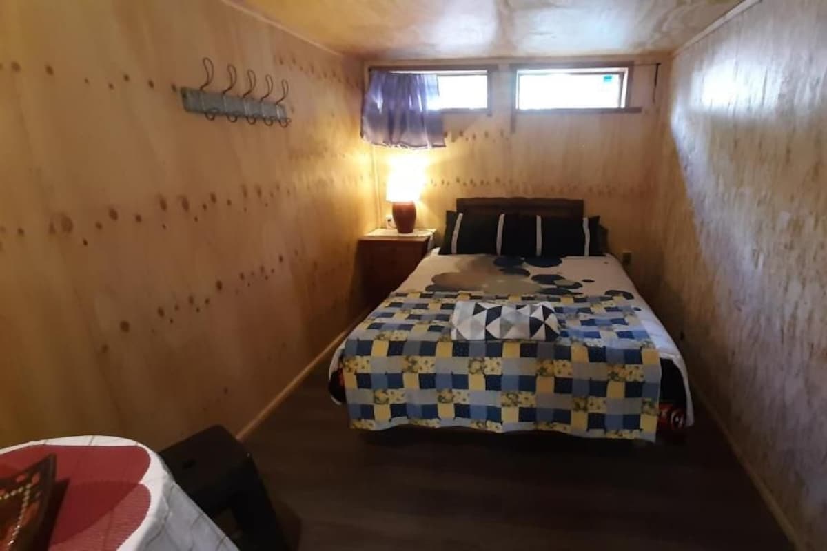 Een kleine, knusse kamer met een bed, nachtkastje, lamp en raam.