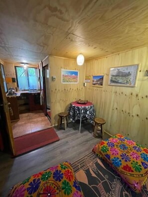 A wooden room with a bed, a small table with stools, and a door leading to another room.