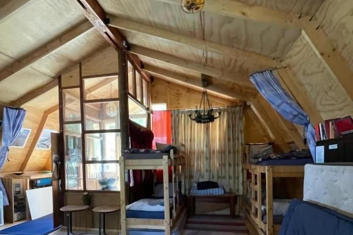 Een knus zolderkamer met een schuine kap, een stapelbed, een bureau en een kleine tafel.
