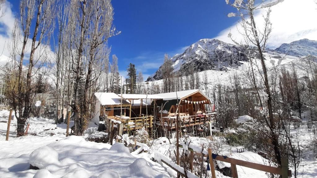 Un chalet en bois, dont le toit est recouvert de neige, entouré d’arbres chargés de neige et avec des montagnes en arrière-plan.
