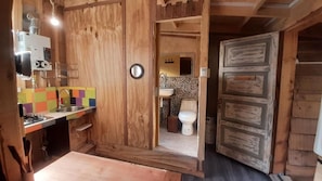 Een houten interieur met een keukenhoek, een spoelbak en een toilet dat door een open deur zichtbaar is.