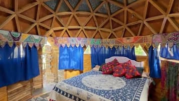 A room with a geometric wooden ceiling, a bed with patterned bedding, and blue curtains.