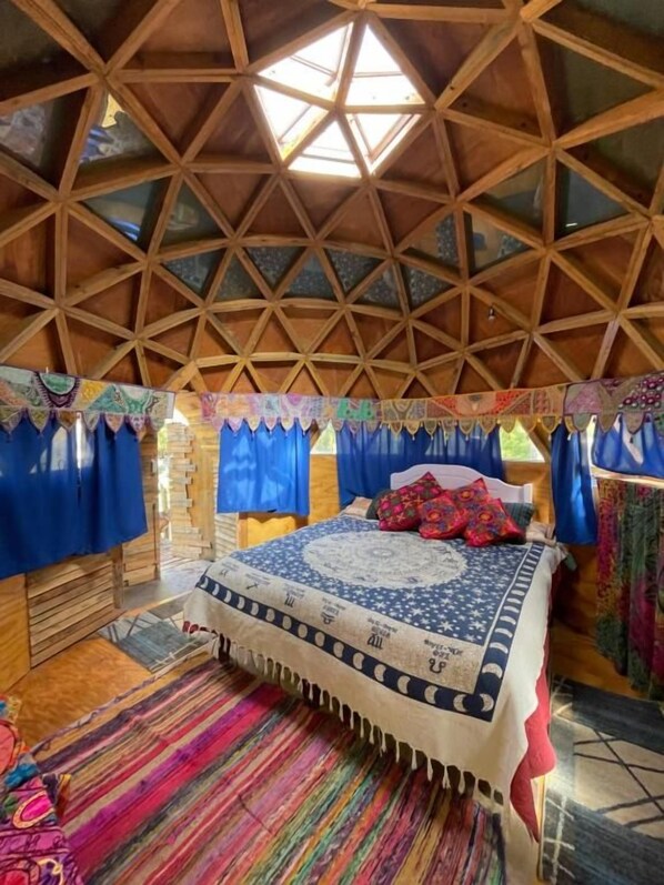 A room with a geometric wooden ceiling, a bed with patterned bedding, and blue curtains.