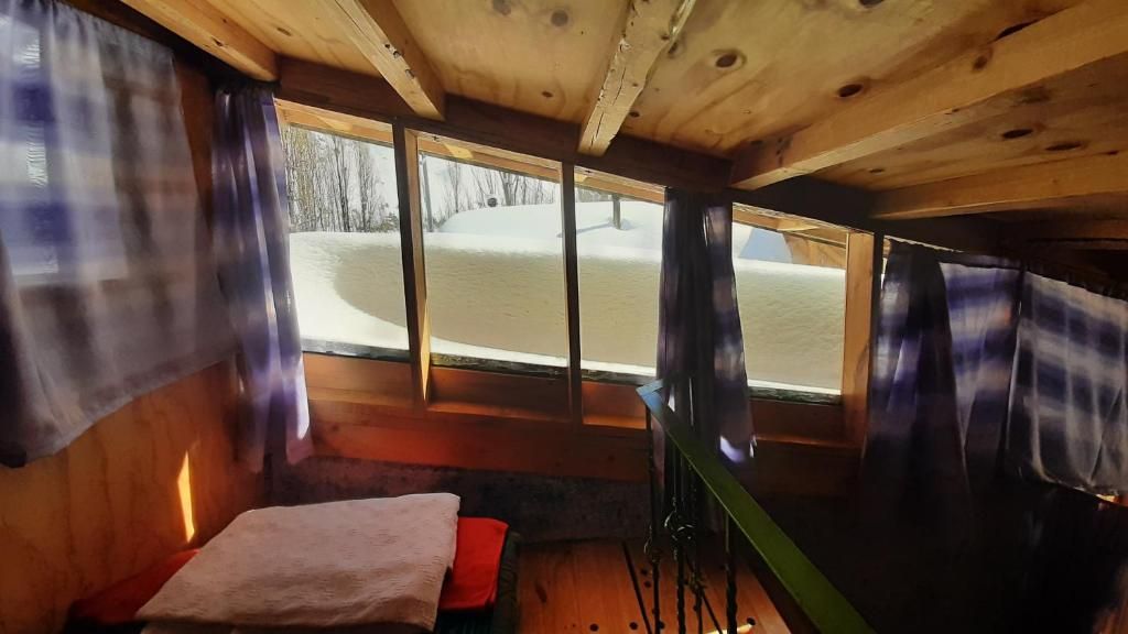 A cabin interior with a bed, a window, and a view of a snowy landscape.