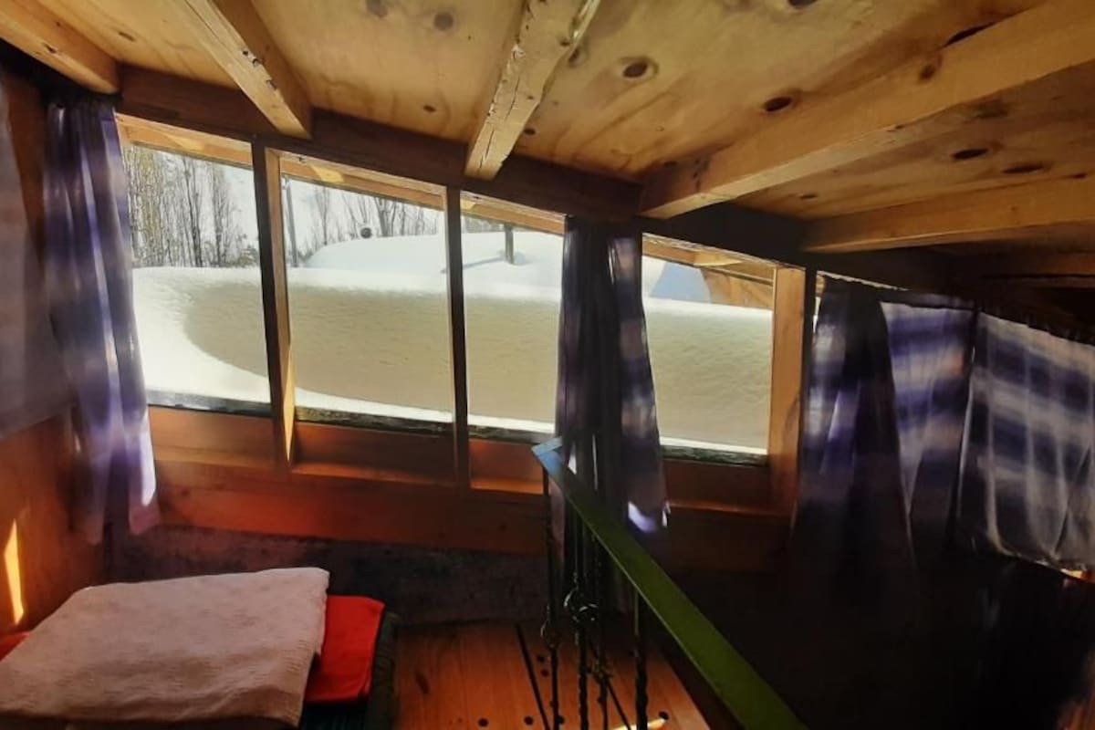 Een blokhutinterieur met een bed, een raam en uitzicht op een besneeerd landschap.