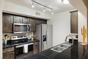 A modern kitchen with stainless steel appliances, dark wooden cabinets, and a black countertop. - Private Pool, Patio TV, 15-min to Old Town (Phoenix)