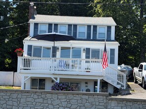 A two-story house with a balcony, a flag, and a stone wall in front. - Lake House 3-bedroom on lake Beseck Middlefield (Middlefield)