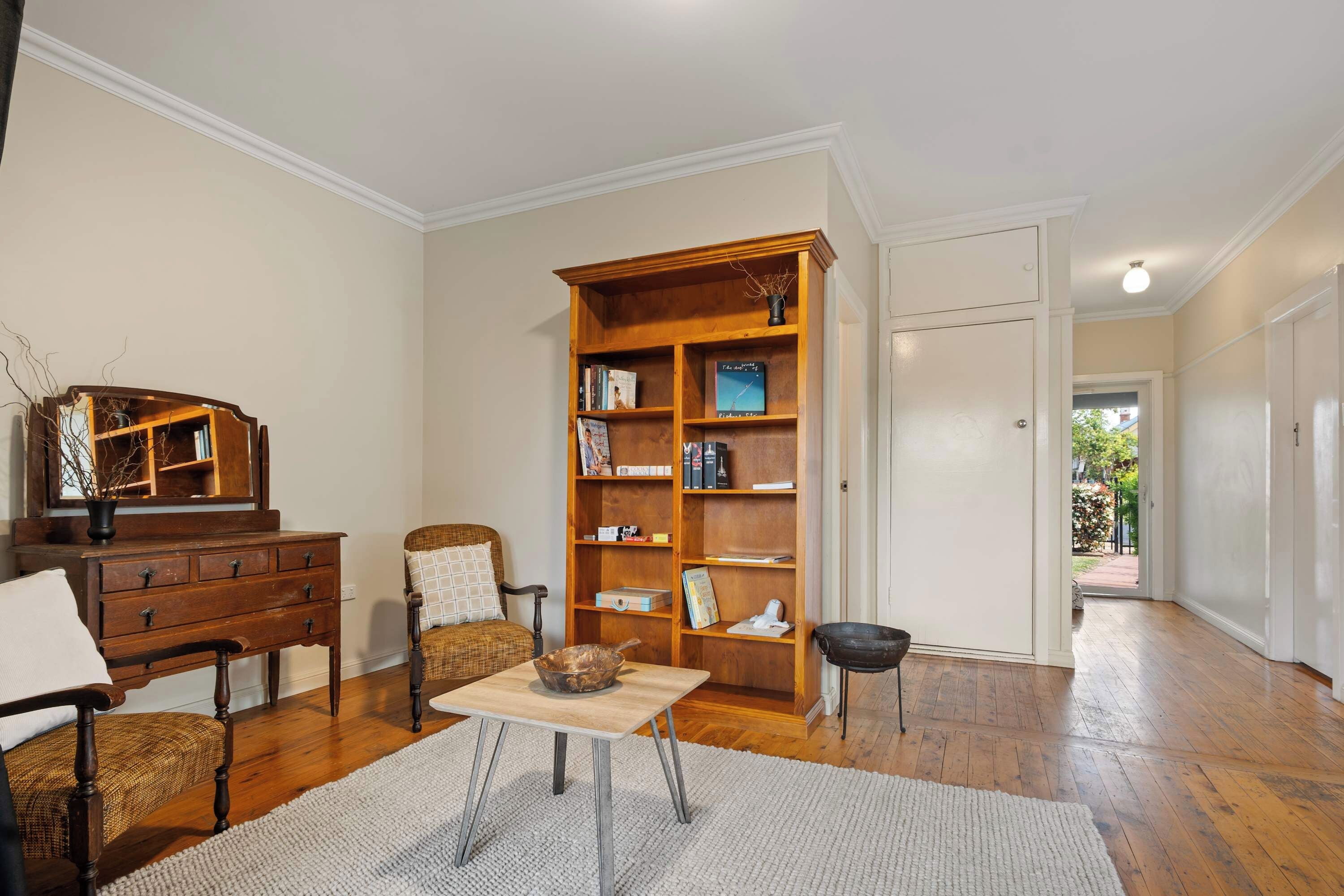 A room with a wooden bookshelf, a chair, a small table, and a mirror.