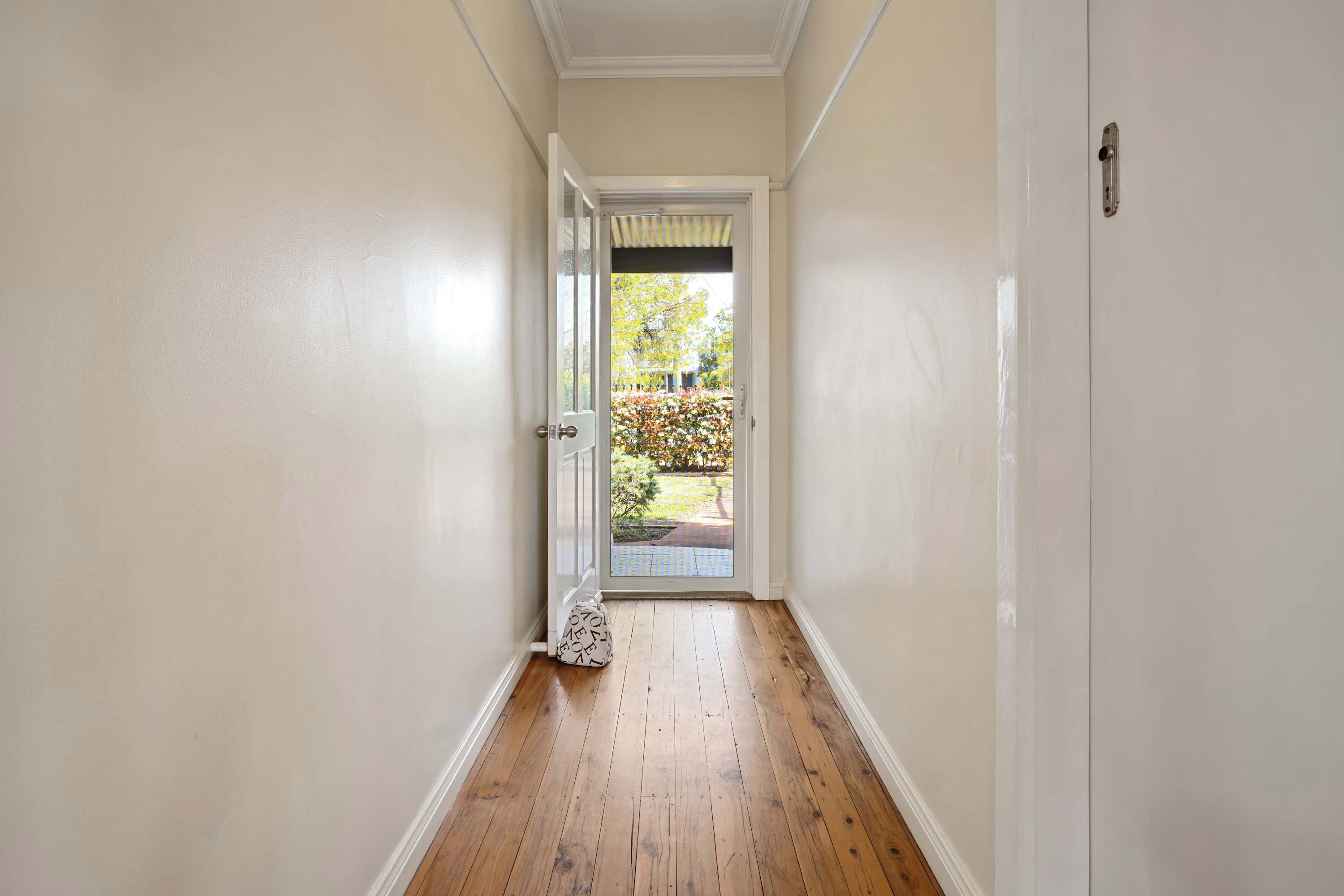 A hallway with a wooden floor and a door leading to an outdoor area with a garden.