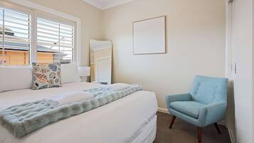 A hotel room with a bed, a chair, a window with blinds, a door, and a wall-mounted artwork.