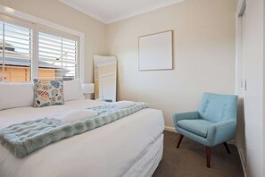 A hotel room with a bed, a chair, a window with blinds, a door, and a wall-mounted artwork. - Quinn House A Honey Home (Dubbo)