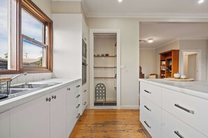 A modern kitchen with white cabinetry, a wooden floor, and a window. - Quinn House A Honey Home (Dubbo)
