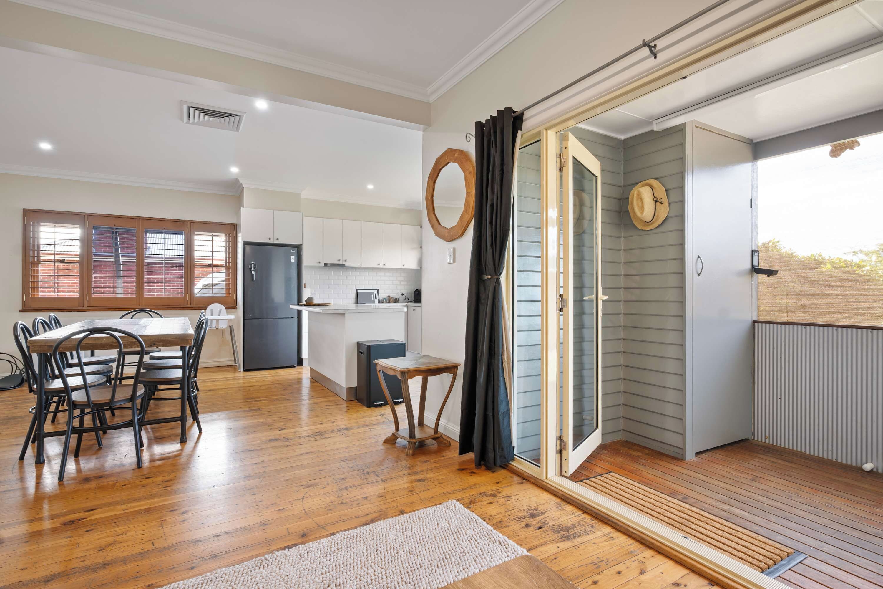A spacious kitchen with white cabinets, a dining area with a wooden table and chairs, and a sliding glass door leading to a balcony.