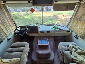 A vehicle's interior with a steering wheel, dashboard, and two cushioned seats. - Cozy 1-bedroom recreational vehicle in awesome Lucedale with AC (Lucedale)