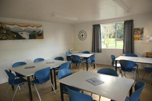 Una habitación con paredes blancas, un reloj y una ventana con cortinas. Hay mesas y sillas dispuestas para sentarse.