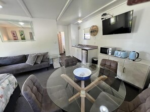 Una sala de estar moderna con una mesa de comedor de vidrio, un sofá, un televisor y una cocina equipada con microondas y tostadora.
