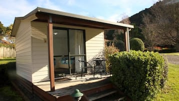 A small, single-story building with a porch, a sliding glass door, and a set of outdoor furniture.