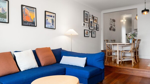 Ein Wohnzimmer mit einem blauen Sofa, einem runden Couchtisch und einem Essbereich mit einem weißen Tisch und Holzstühlen.