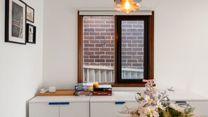Ein Zimmer mit Fenster, einem weißen Schreibtisch und einer Blumenvase.