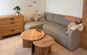 Un salón acogedor con un sofá gris, un aparador de madera, una mesita redonda de madera y una planta en maceta.