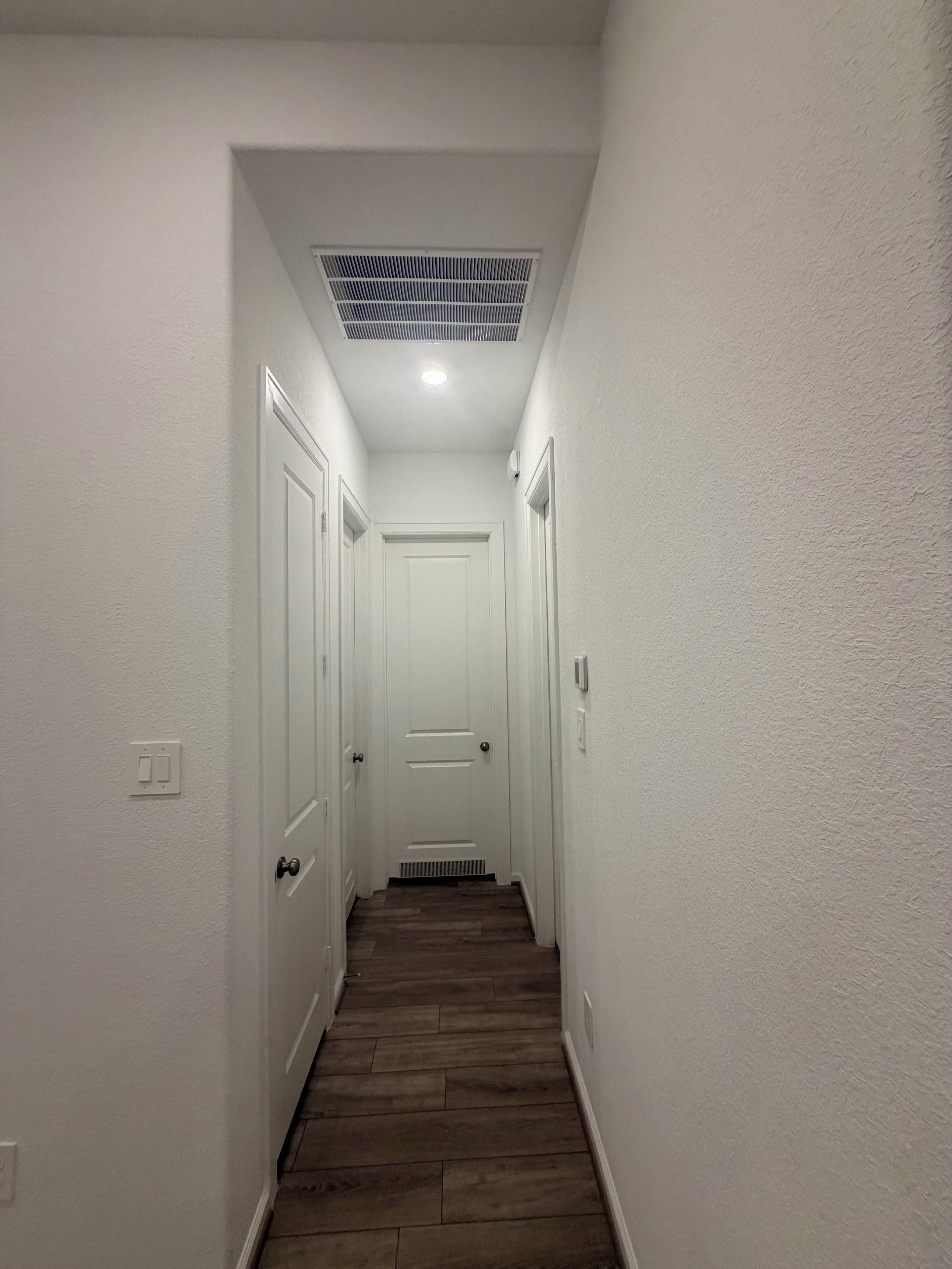 A narrow hallway with white walls, a wooden floor, and a white door at the end.