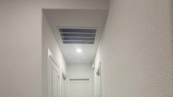Un couloir étroit aux murs blancs, avec un plancher en bois et une porte blanche au fond.