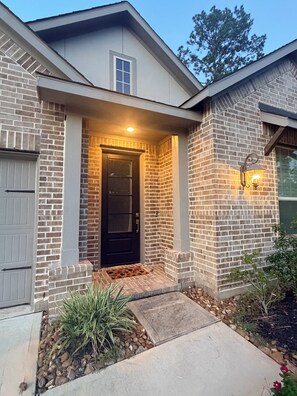 A residential house with a brick exterior, a front door, a small porch, and a light fixture.