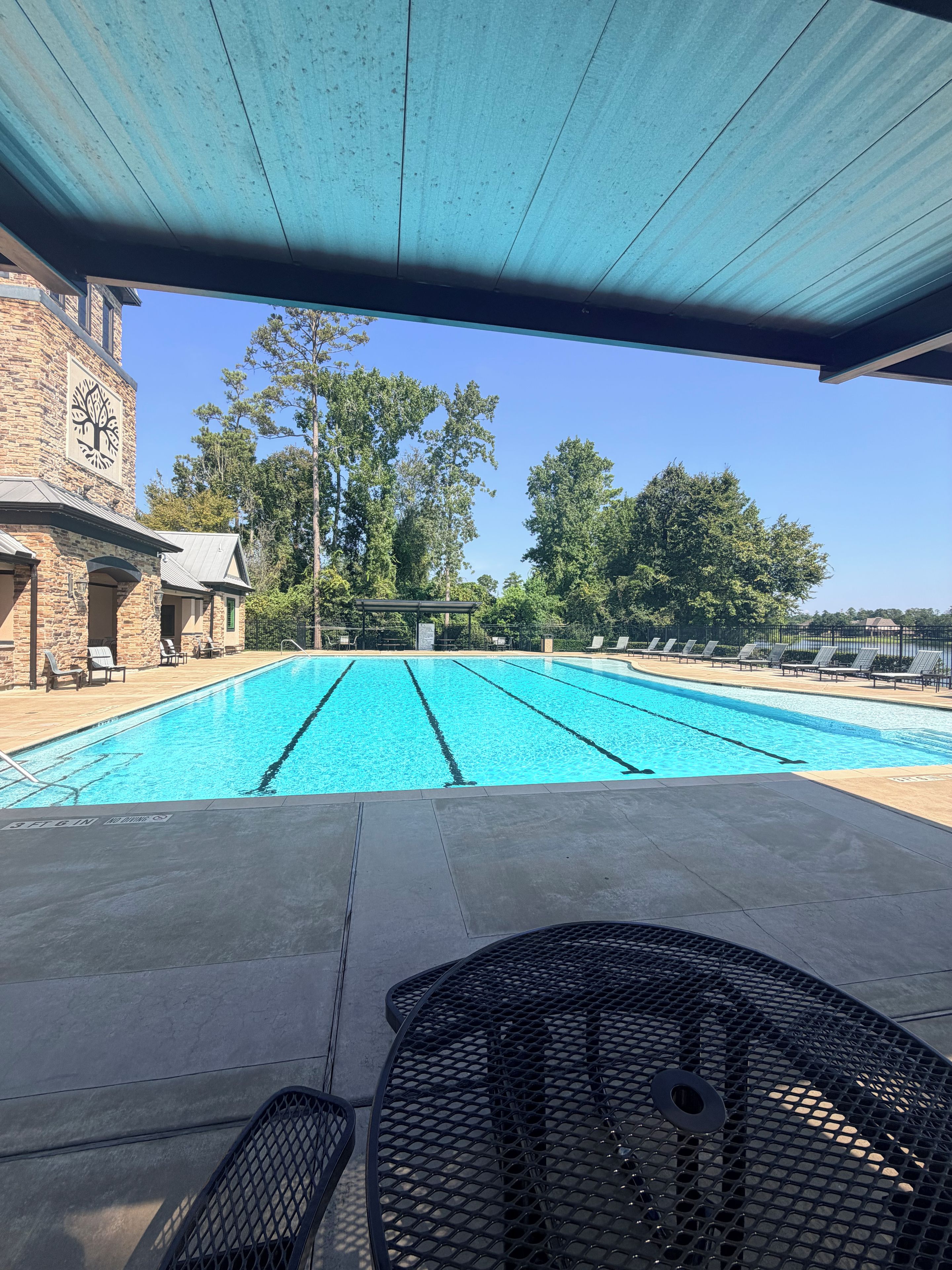 A swimming pool with clear blue water, surrounded by lounge chairs and a covered patio area.