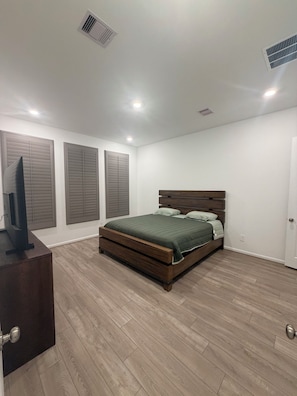 A bedroom with a bed, a television on a stand, and a door.