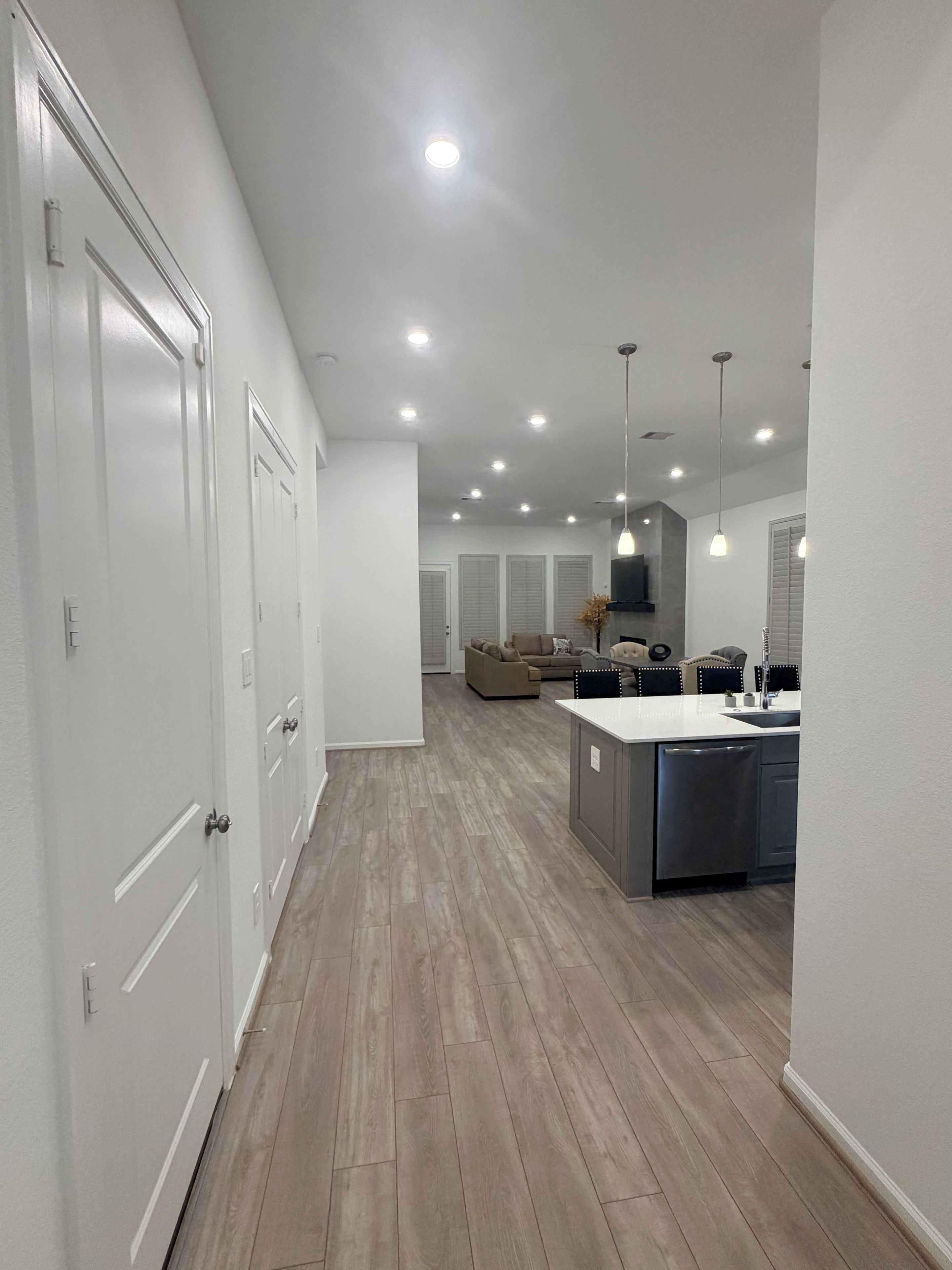 A modern kitchen with a central island, recessed ceiling lights, and a hallway with white doors.