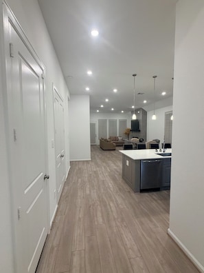 Cozinha moderna com ilha central, iluminação embutida no teto e corredor com portas brancas.
