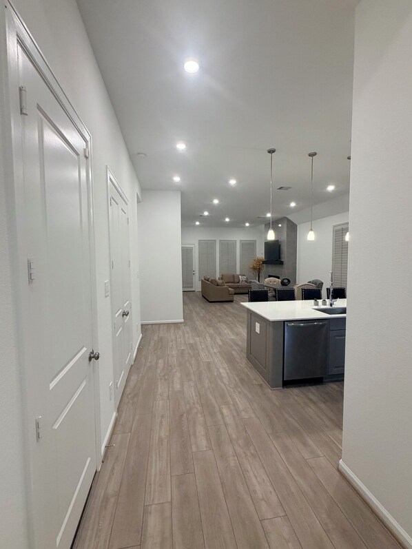 A modern kitchen with a central island, recessed ceiling lights, and a hallway with white doors.