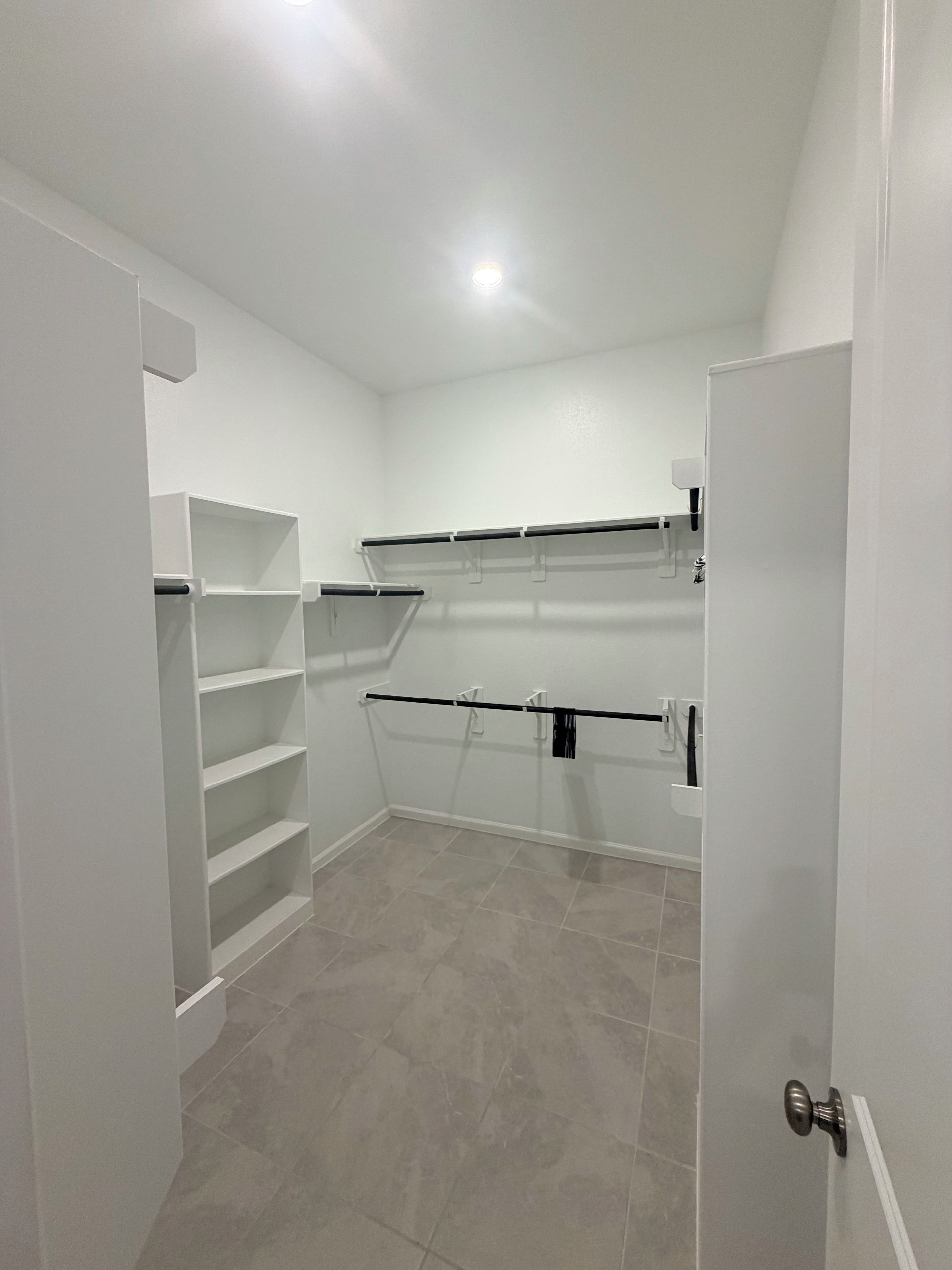 A room with white walls, a tiled floor, and a door with a silver handle.