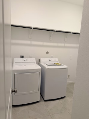 Uma lavanderia com duas máquinas de lavar de carregamento frontal brancas e uma prateleira de metal acima delas.